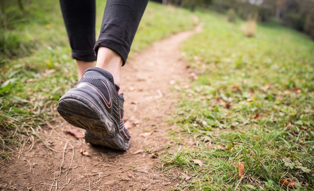Close-up of a person walking on a dirt path in nature, wearing athletic shoes, symbolizing a healthy lifestyle and mindful movement.