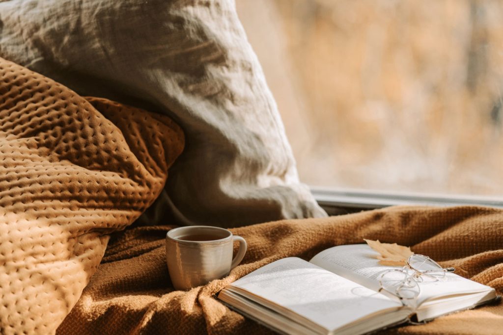 Cozy reading nook with a warm blanket, a cup of tea, an open book, and eyeglasses—representing reflection and quiet time for personal new year resolution ideas.