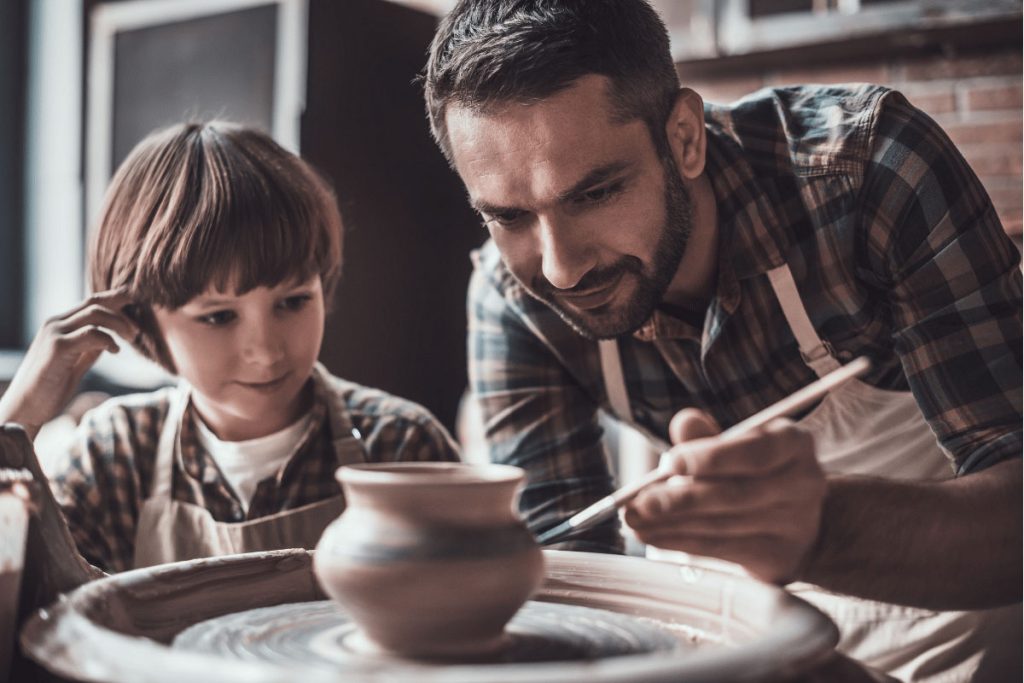 Father and child engaged in pottery-making, wearing aprons and focused on decorating a clay pot—representing creative hobbies and hands-on new year resolution ideas.