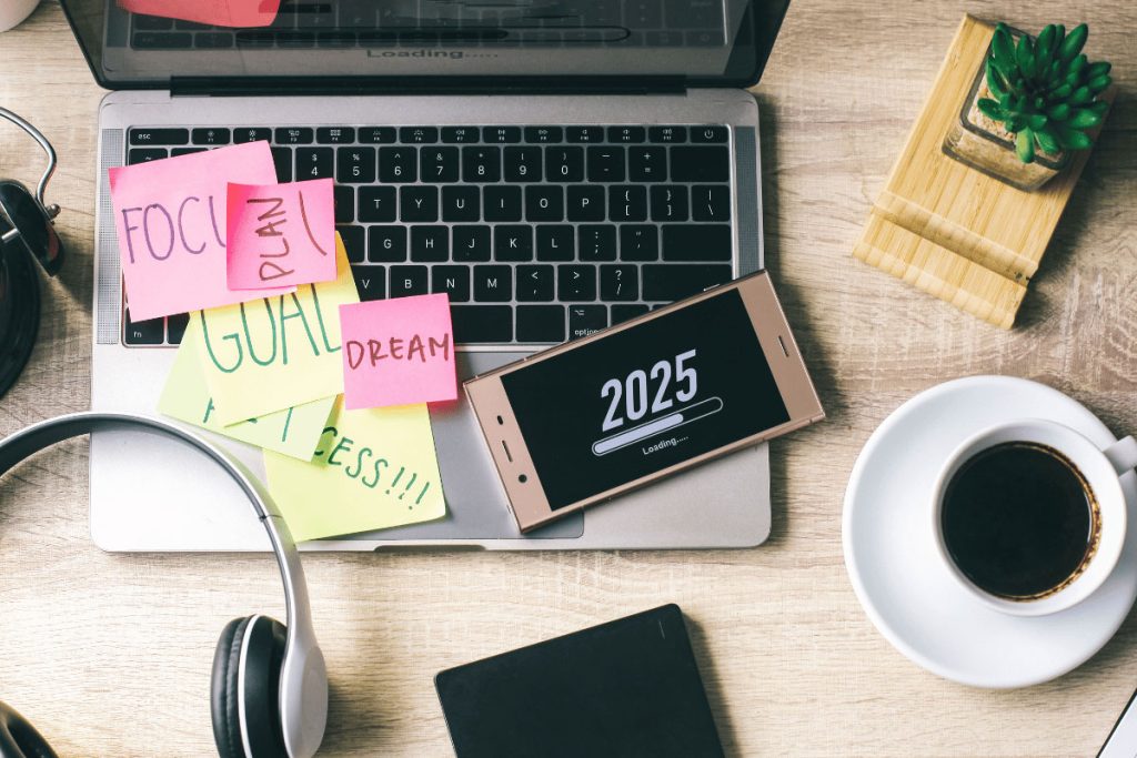 Laptop with sticky notes labeled “Focus,” “Plan,” “Goal,” and “Dream,” next to a phone showing “2025 loading”—a visual cue for new year resolution ideas.