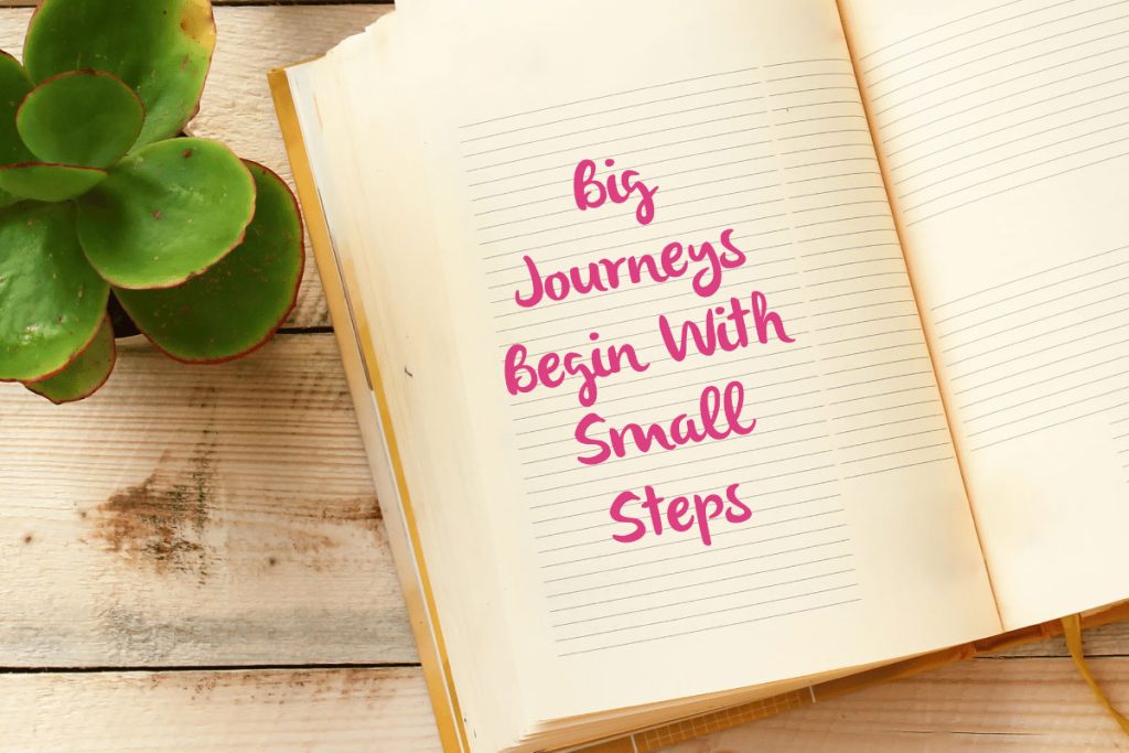 Open journal with the words “Big Journeys Begin With Small Steps” written in pink, placed beside a succulent on a wooden surface—symbolizing motivation and new year resolution ideas.