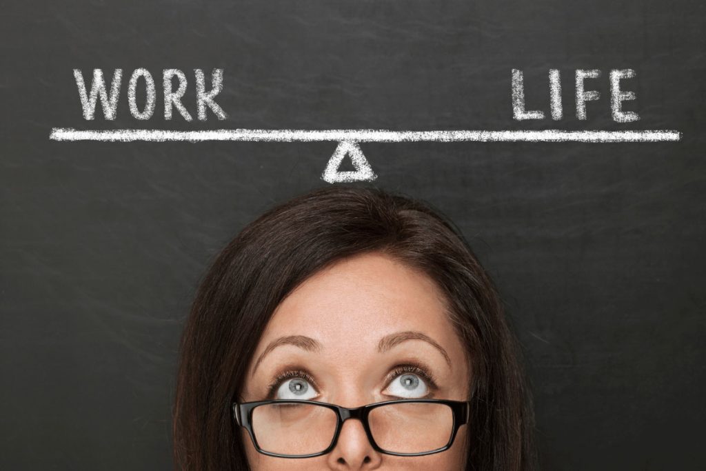 Woman looking up at a chalkboard with the words “Work” and “Life” balanced on a seesaw line—illustrating the concept of work-life balance as part of new year resolution ideas.